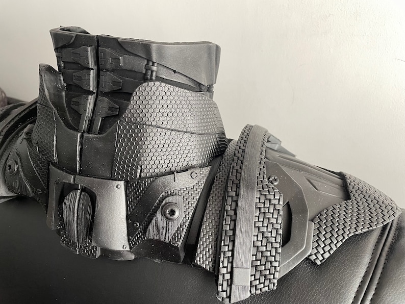 May include: Black and gray 3D printed costume piece with a textured surface and intricate details. The piece has a collar and shoulder armor design.