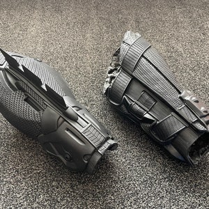 May include: Two black plastic arm guards with textured surfaces. One guard has a pointed, blade-like extension.