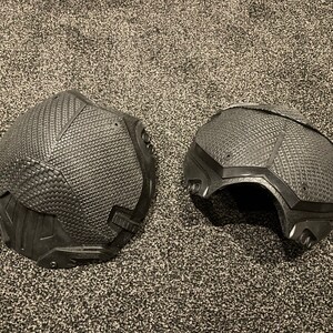 May include: Two black, textured, helmet-like pieces, possibly for cosplay or costume use. The pieces are made of a material that resembles moulded plastic or rubber.