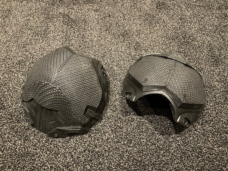 May include: Two black, textured, helmet-like pieces, possibly for cosplay or costume use. The pieces are made of a material that resembles moulded plastic or rubber.