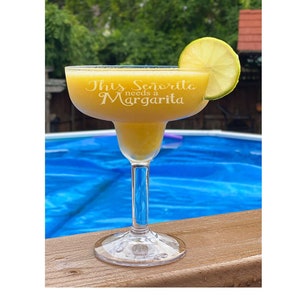 May include: A margarita glass with a yellow drink and a lime wedge on the rim. The glass is etched with the text "This Senorita needs a Margarita".