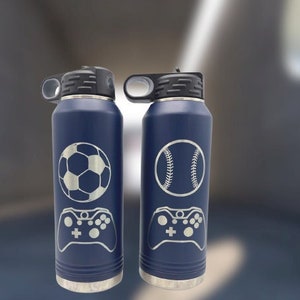 May include: Two stainless steel water bottles with a navy blue finish. The bottles have a black lid and a carrying handle. One bottle has a soccer ball and a video game controller engraved on it. The other bottle has a baseball and a video game controller engraved on it.