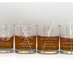May include: Four clear glass tumblers with engraved quotes about quantum mechanics. The quotes are by Erwin Schrodinger, John Wheeler, and Richard Feynman. The tumblers are filled with a brown liquid.