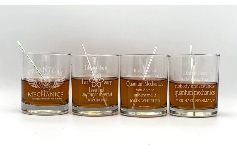 May include: Four clear glass tumblers with engraved quotes about quantum mechanics. The quotes are by Erwin Schrodinger, John Wheeler, and Richard Feynman. The tumblers are filled with a brown liquid.