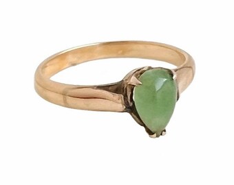 May include: A gold ring featuring a pear-shaped, light green gemstone. The ring has a simple band and a setting that cradles the gemstone. The gemstone is approximately 0.75 inches in length.