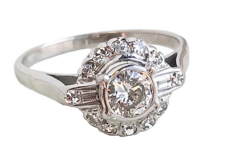 May include: A silver ring with a large round diamond surrounded by smaller diamonds. The ring has a delicate band and a halo setting.