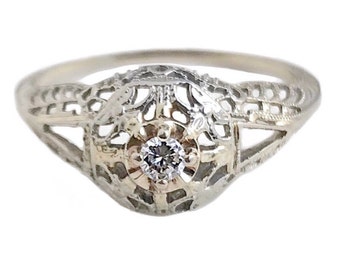 May include: A delicate silver ring with a filigree design and a single round diamond in the center.