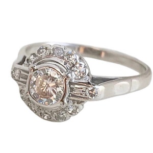 May include: A silver ring with a large round diamond surrounded by smaller diamonds. The ring has a delicate band and a halo setting.