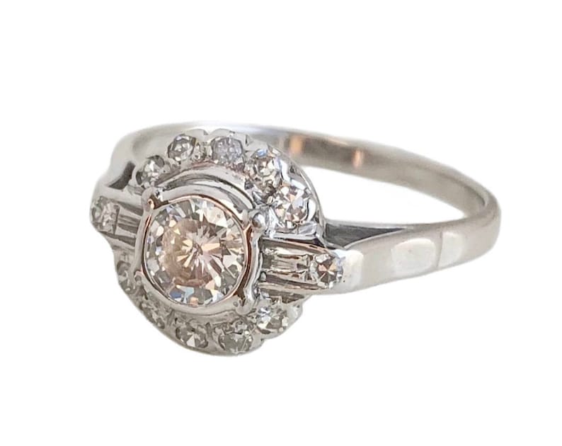 May include: A silver ring with a large round diamond surrounded by smaller diamonds. The ring has a delicate band and a halo setting.