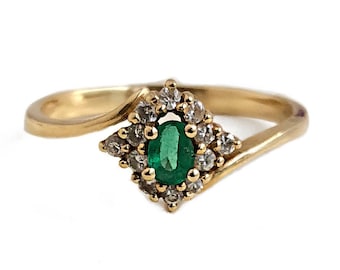 May include: A gold ring with a green emerald gemstone surrounded by smaller diamonds.