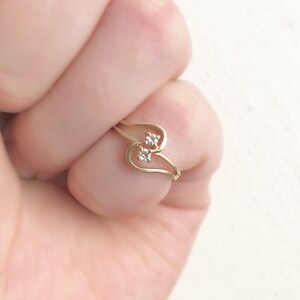May include: A gold ring with two small clear stones set in a heart shape.