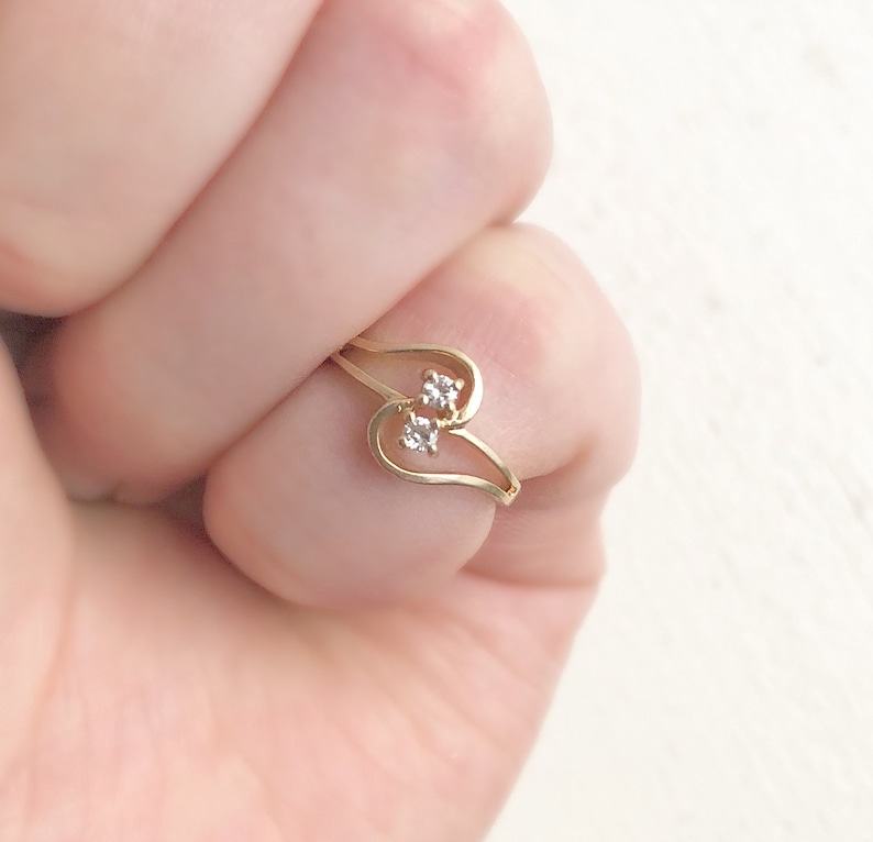 May include: A gold ring with two small clear stones set in a heart shape.