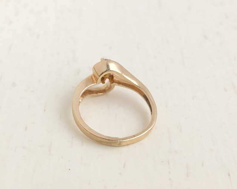 May include: A gold ring with a single stone set in a heart-shaped design.