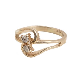 May include: A gold ring with two small diamonds set in the band. The ring is designed in a twisted, heart-shaped pattern.