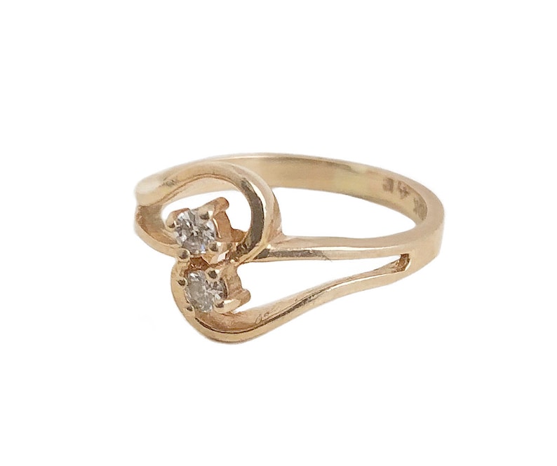 May include: A gold ring with two small diamonds set in the band. The ring is designed in a twisted, heart-shaped pattern.
