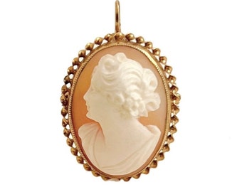 May include: A gold-toned oval cameo pendant featuring a carved profile of a woman with a detailed hairstyle. The cameo is set in a delicate gold-toned frame with a beaded edge.