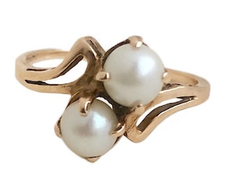 May include: A gold ring with two white pearls set in a swirling design.