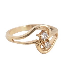 May include: A gold ring with a delicate, curved design and two small, clear gemstones.