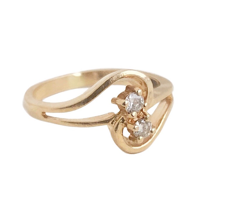 May include: A gold ring with a delicate, curved design and two small, clear gemstones.