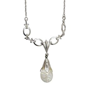 May include: A silver-toned necklace with a delicate design. The necklace features a chain with decorative links and a pendant shaped like a teardrop. The pendant contains a clear, iridescent stone, adding a touch of sparkle.