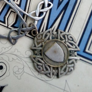 May include: A collection of necklaces and pendants on a vintage book. One necklace features light green beads and silver accents. Another has a heart charm and key. A silver pendant with a Celtic knot design is also present.