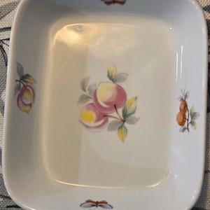 May include: A white square ceramic dish with a raised rim. The dish has a floral design with pink peaches and butterflies.