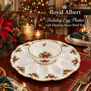 May include: A white porcelain Royal Albert Holiday Egg Platter with a matching dipping sauce bowl set. The platter features scalloped edges, gold trim, and a festive holly and red ribbon pattern. The bowl sits in the center of the platter.