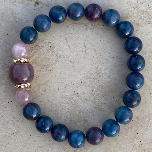 May include: A blue and purple gemstone bracelet with a pink and gold charm. The bracelet is made of round beads and is strung on elastic.