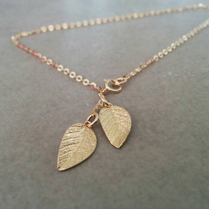 May include: A delicate gold chain necklace with two small gold leaf charms hanging from it.
