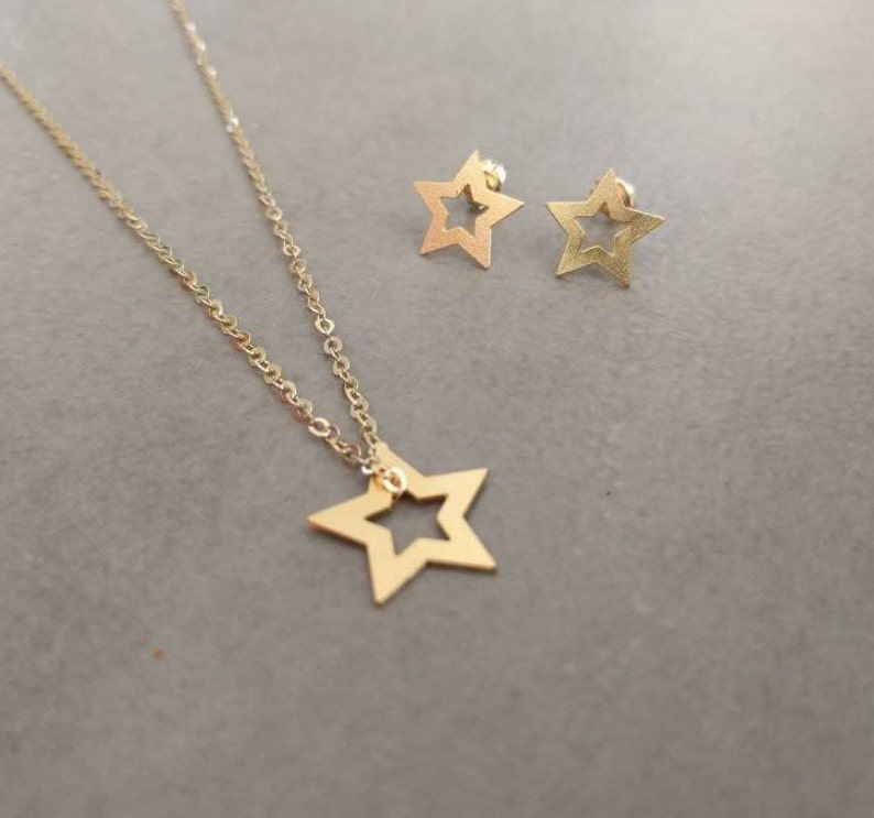 May include: A gold necklace and earrings set featuring a star pendant and matching earrings. The star pendant and earrings have a cutout design.
