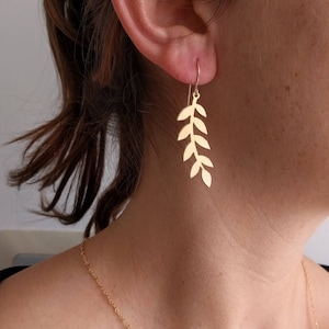 Pu&ograve; includere: Orecchini a foglia d'oro con un delicato design a ramo. Gli orecchini sono lunghi e pendono dal lobo dell'orecchio.