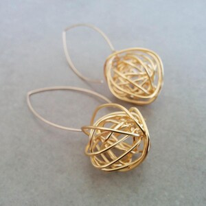 May include: A pair of gold-toned earrings with a delicate wire design. The earrings are shaped like a sphere and have a dangling drop design.