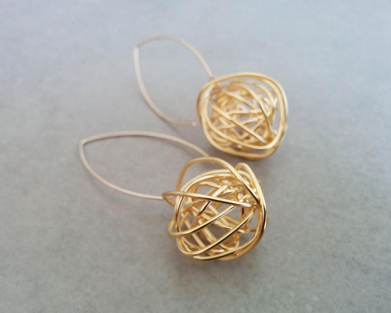 May include: A pair of gold-toned earrings with a delicate wire design. The earrings are shaped like a sphere and have a dangling drop design.