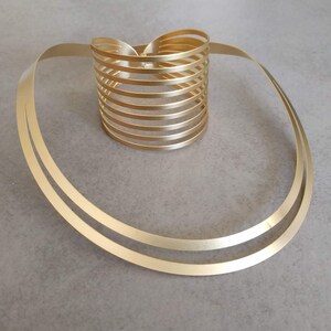 May include: A gold-toned metal necklace with a thick, double-layered chain and a matching, multi-layered cuff bracelet.