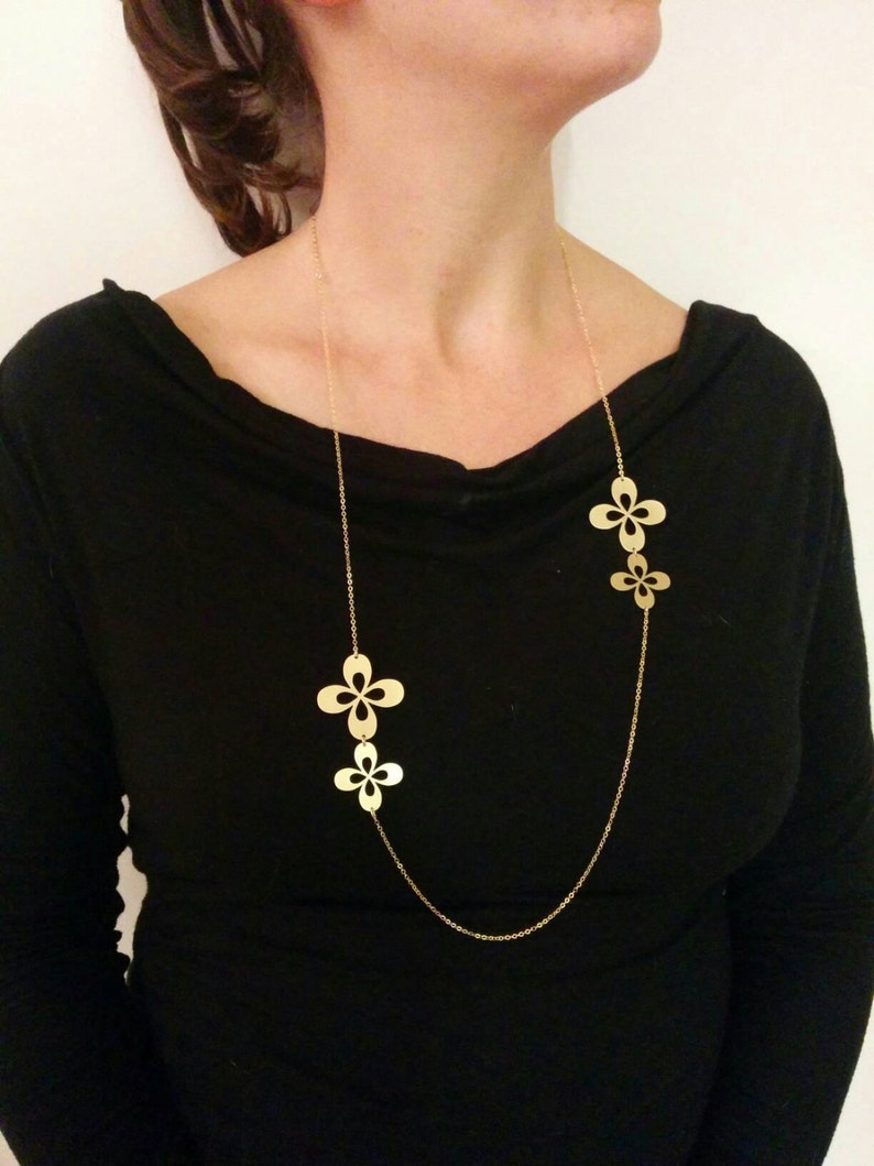 May include: A gold chain necklace with three flower-shaped pendants. The necklace is on a model wearing a black shirt.
