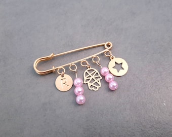 Può includere: Spilla di sicurezza dorata con ciondoli, tra cui una mano di hamsa, una stella, una lettera R e perline rosa.