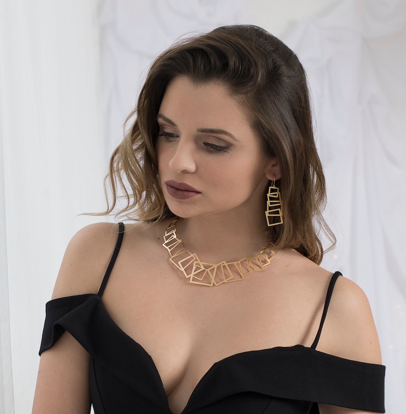 May include: A woman wearing a black off-the-shoulder dress with a gold geometric necklace and matching earrings.