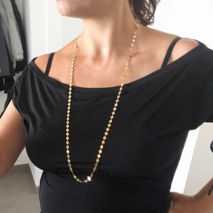 Puede incluir: Un collar de cadena de oro con un patr&oacute;n de eslabones cuadrados. El collar es largo y cuelga hasta el pecho.