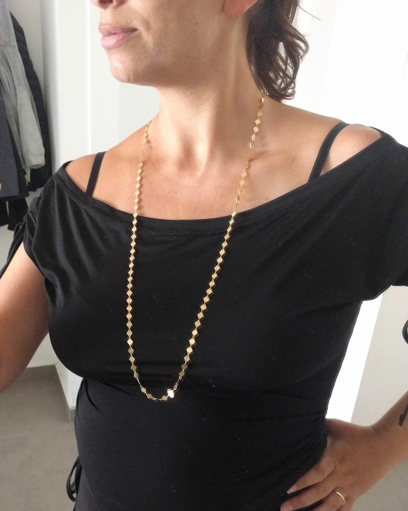 Puede incluir: Un collar de cadena de oro con un patr&oacute;n de eslabones cuadrados. El collar es largo y cuelga hasta el pecho.
