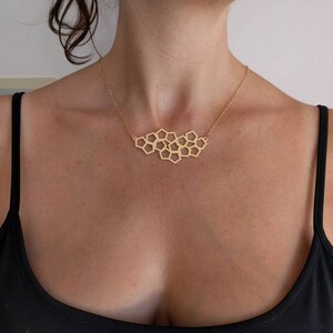 Pu&ograve; includere: Una collana d'oro con un ciondolo geometrico a forma di nido d'ape. La collana &egrave; indossata da una persona con una canotta nera.