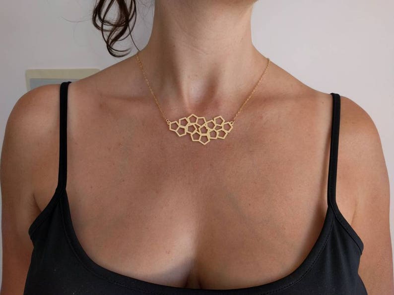 Pu&ograve; includere: Una collana d'oro con un ciondolo geometrico a forma di nido d'ape. La collana &egrave; indossata da una persona con una canotta nera.