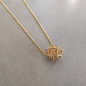 May include: A gold chain necklace with a delicate, intricate, spherical pendant.
