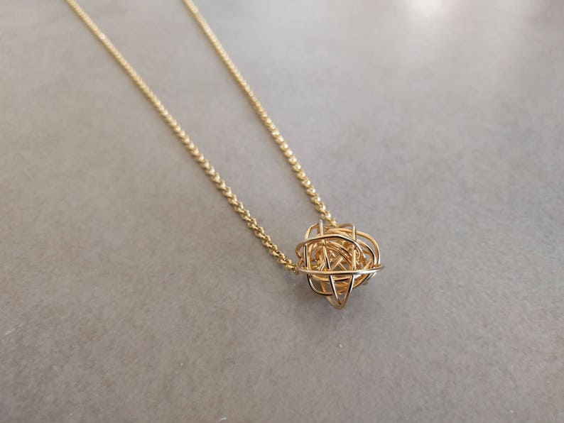 May include: A gold chain necklace with a delicate, intricate, spherical pendant.