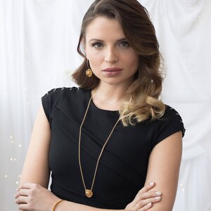 May include: A woman wearing a black dress with a gold chain necklace and matching earrings. The necklace and earrings feature a circular design.