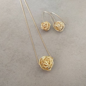 May include: A gold necklace and earrings set with a delicate chain and a round, wire-wrapped pendant. The pendant and earrings are made of a woven wire design.
