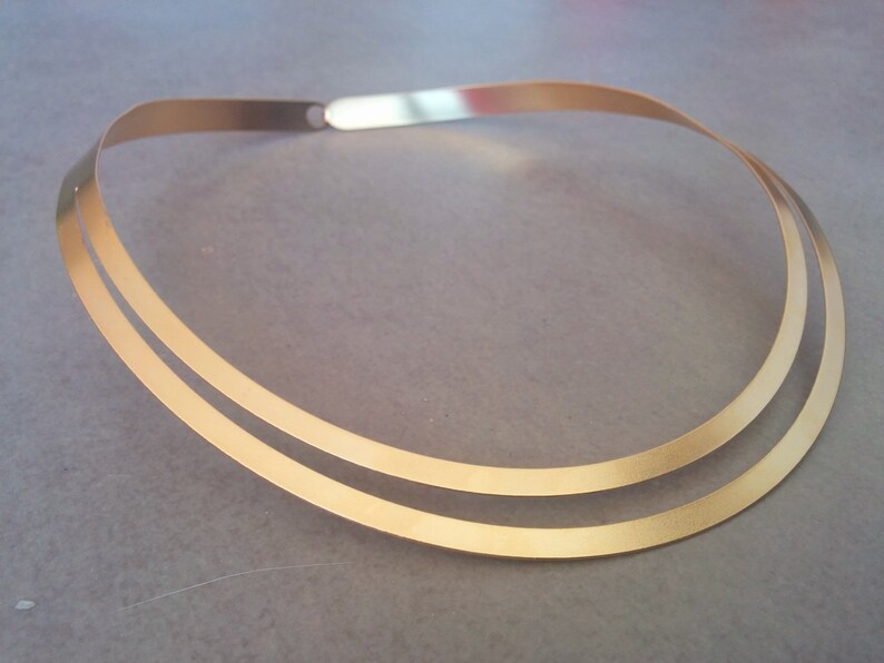 May include: A gold-toned double-layered choker necklace. The necklace is made of two thin, flat bands of metal that are joined together at the back.