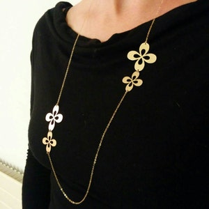 May include: A gold chain necklace with three flower-shaped pendants. The necklace is worn by a person wearing a black shirt.