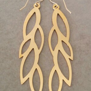 May include: A pair of gold-toned earrings with a leaf design. The earrings are long and dangle, with multiple cutouts in the shape of leaves.