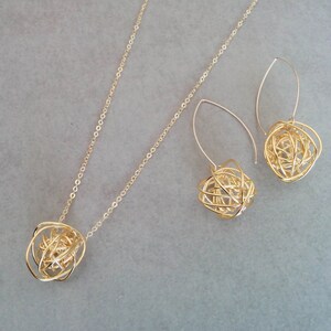 May include: A gold necklace and earrings set with a delicate chain and a pendant and earrings featuring a gold wire sphere design.