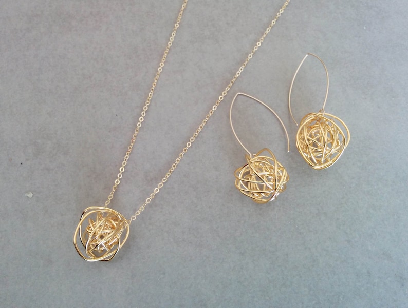May include: A gold necklace and earrings set with a delicate chain and a pendant and earrings featuring a gold wire sphere design.